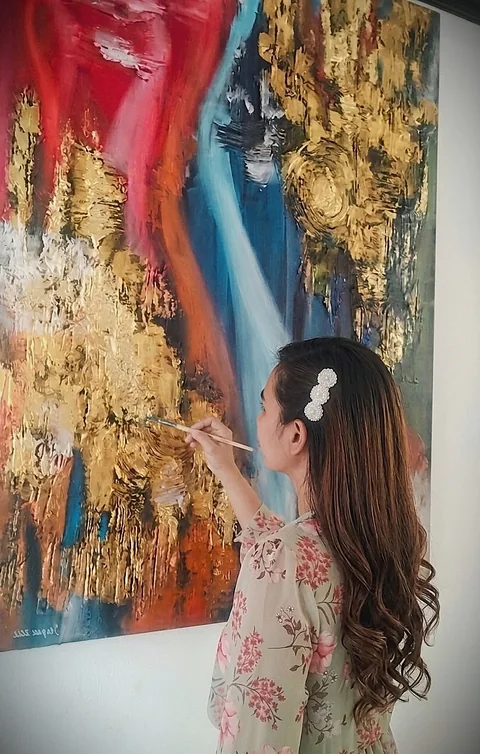 Artist Yen Pace painting a large gold, red and blue textured abstract canvas in her studio